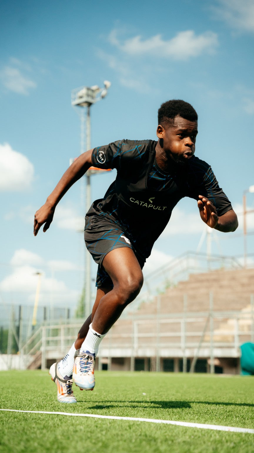 Footballeur en pleine accélération sur le terrain, avec chaussettes blanches et crampons.