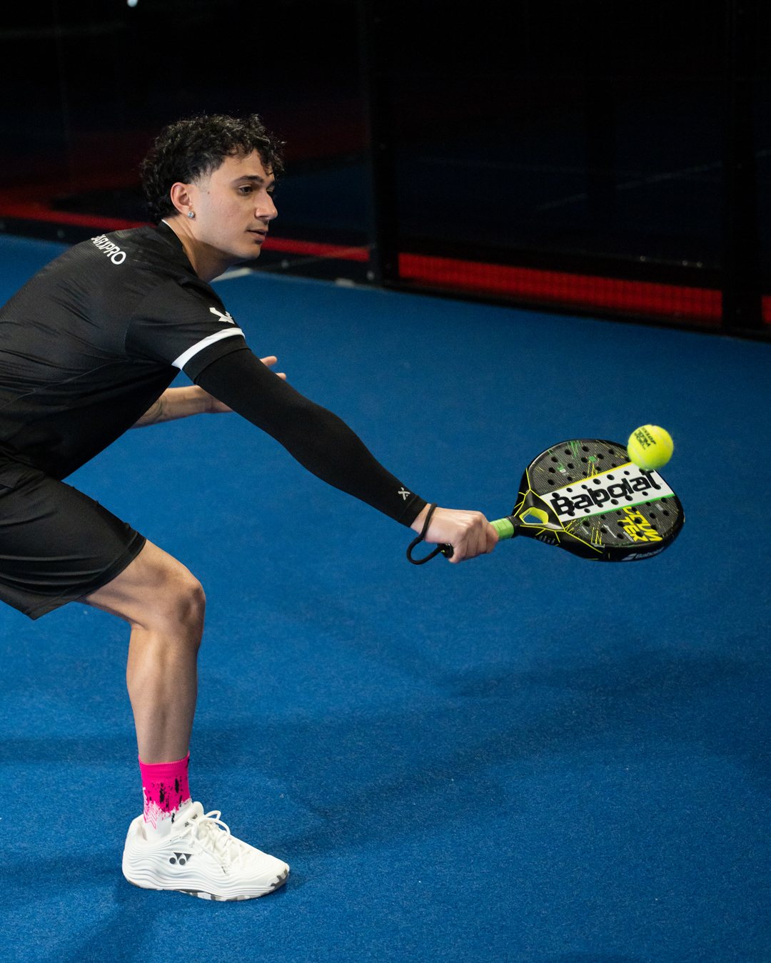 Padel-Spieler beim tiefen Volley mit schwarzer Arm Sleeve